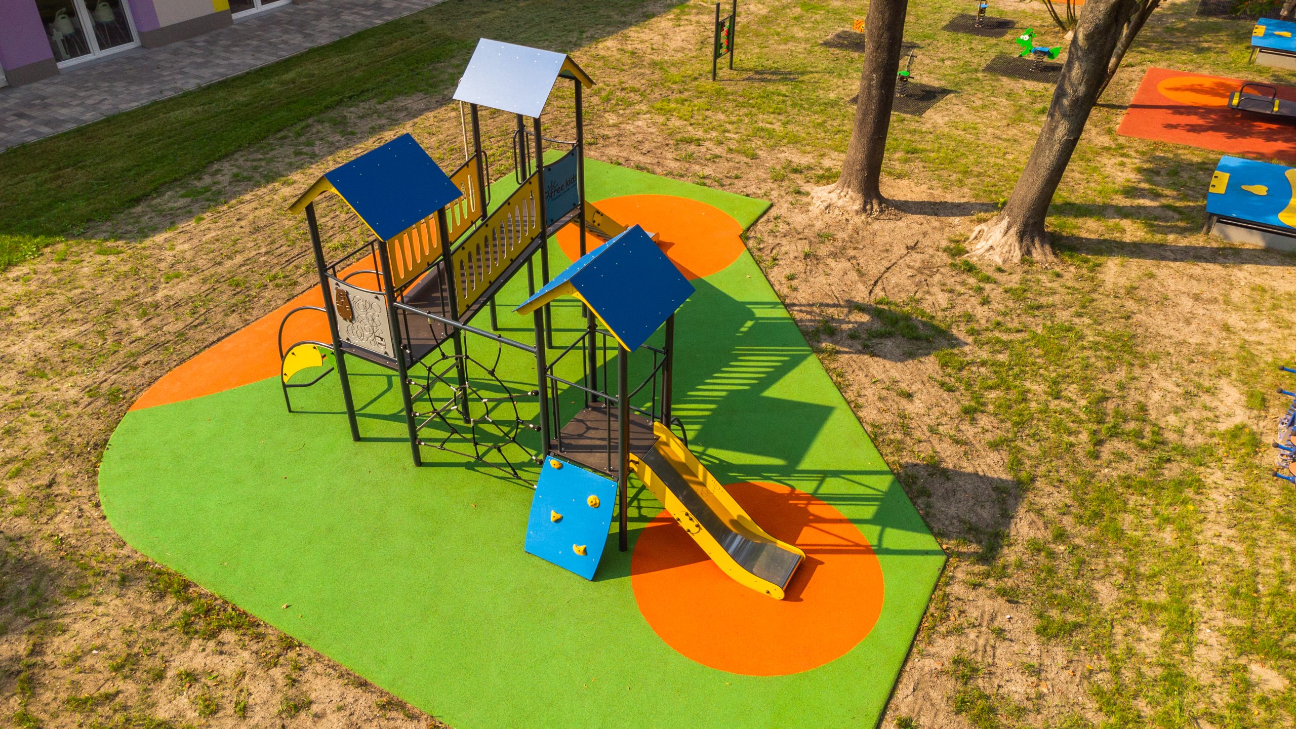 Nowoczesne zjeżdżalnie i urządzenia wspinaczkowe: jak projektować place zabaw, które naprawdę angażują? Zjeżdżalnie i urządzenia wspinaczkowe to klasyka, która nigdy się nie starzeje. Choć zmieniają się materiały, technologie i trendy, jedno pozostaje niezmienne – dzieci kochają wspinać się i zjeżdżać. Współczesne place zabaw wykorzystują te elementy nie tylko do zabawy, ale także do wspierania rozwoju dzieci: fizycznego, społecznego i emocjonalnego. Ten artykuł pokaże Ci, jak różnorodne mogą być zjeżdżalnie i urządzenia wspinaczkowe, co dają dzieciom i jak projektować je tak, by były dostępne, bezpieczne i ekscytujące. Bo plac zabaw to nie tylko sprzęt – to miejsce, które żyje, pulsuje śmiechem i buduje więzi. Jakie są rodzaje nowoczesnych zjeżdżalni? Zjeżdżalnie to coś więcej niż tylko gładki tor do szybkiego ślizgu. Mamy tu różnorodność, która potrafi zaskoczyć. Klasyczne proste zjeżdżalnie są świetne dla najmłodszych, bo uczą podstaw – kontrolowania pozycji ciała, równowagi i odwagi. Z kolei zjeżdżalnie faliste wprowadzają dodatkowe bodźce sensoryczne – delikatne podskoki, rytmiczne wibracje, które rozbudzają ciekawość. Warto też pamiętać, że odpowiednia wysokość i kąt nachylenia muszą być dopasowane do wieku dziecka, by maluch mógł zjechać bezpiecznie, ale z emocjami. Są też spiralne zjeżdżalnie, które mieszczą się na mniejszej przestrzeni, ale oferują dłuższą trasę i wymagają od dziecka lepszej orientacji w przestrzeni. Tunelowe zjeżdżalnie dodają element zaciszności, a zjeżdżalnie równoległe pozwalają bawić się wspólnie, ścigając się z kolegami. Nowością są też zjeżdżalnie rolkowe, które oprócz ślizgu oferują intensywne doznania dotykowe i dźwiękowe, przyciągając starsze dzieci szukające nowych wrażeń. Urządzenia wspinaczkowe – nie tylko dla starszaków Wspinaczka to jeden z najbardziej wszechstronnych rodzajów aktywności na placu zabaw. Dla młodszych dzieci przygotowuje się niskie konstrukcje z łatwymi uchwytami, gdzie mogą ćwiczyć koordynację i planowanie ruchów. Dla starszych wchodzą do gry siatki, drabinki, ściany wspinaczkowe i geometryczne konstrukcje. Każdy stopień trudności pozwala dzieciom rozwijać siłę, uczyć się pokonywania strachu i zdobywać poczucie sprawczości. A nic tak nie buduje pewności siebie, jak pokonanie przeszkody, która wcześniej wydawała się nie do przejścia. Nie można zapominać o wspinaczce inspirowanej naturą – sztuczne głazy, pieńki, drewniane platformy – to nie tylko trening fizyczny, ale też sposób na rozwijanie wyobraźni i kontakt z naturalnymi materiałami. Coraz popularniejsze są także wieże linowe czy piramidy z siatek, które stawiają przed dziećmi wyzwania na wielu poziomach trudności, a przy tym pozwalają na zabawę grupową i budowanie relacji z rówieśnikami. Co daje dzieciom zabawa na zjeżdżalniach i wspinaczce? Nie chodzi tylko o rozrywkę. Każdy ślizg, każda wspinaczka to konkretne wsparcie rozwojowe. Zjeżdżalnie stymulują układ przedsionkowy, który odpowiada za równowagę. Ćwiczą też świadomość ciała – dziecko uczy się, jak ułożyć ręce, jak hamować, jak kontrolować prędkość. Co ważne, to zabawa, która przy okazji uczy odwagi i radzenia sobie z emocjami – bo pierwszy samodzielny zjazd bywa dla dziecka prawdziwym przełomem. Wspinaczka rozwija siłę, koordynację i wytrzymałość. To aktywność, która angażuje całe ciało, ale też głowę – trzeba zaplanować trasę, przewidzieć konsekwencje ruchów, ocenić swoje możliwości. Zabawa na wysokości buduje pewność siebie, a każde pokonanie przeszkody wzmacnia wiarę we własne możliwości. Dzieci uczą się tu, jak wytrwać mimo trudności – a to umiejętność przydatna przez całe życie. Nie mniej ważny jest aspekt społeczny. Zjeżdżalnie i urządzenia wspinaczkowe to często centra integracji – dzieci nawiązują tam znajomości, uczą się współpracy, rywalizacji, dzielenia przestrzeni. To miejsca, w których naturalnie rozwijają się umiejętności społeczne. Obserwując dzieci na placu zabaw, widać, jak budują swoje małe społeczności, tworzą zasady, dzielą się rolami – to małe treningi życia w grupie. Jak projektować place zabaw z myślą o bezpieczeństwie i dostępności? Dobry plac zabaw to taki, który łączy emocje z bezpieczeństwem. Wszystkie urządzenia powinny spełniać normy EN 1176, być regularnie kontrolowane i otoczone odpowiednią nawierzchnią amortyzującą. Ważne są także proporcje – nie każdy sprzęt jest dla każdego. Powinny być wydzielone strefy dla najmłodszych, dzieci w wieku szkolnym i tych bardziej zaawansowanych wspinaczy, by każde dziecko znalazło coś dla siebie i czuło się bezpiecznie. Coraz częściej projektanci stawiają na inkluzywność. To oznacza urządzenia, z których mogą korzystać dzieci z niepełnosprawnościami, np. szerokie platformy, łagodne podjazdy, huśtawki z oparciem, transferowe strefy wejścia. Kolorystyka, faktury, różnorodne bodźce sensoryczne – to wszystko ma znaczenie, żeby każdy znalazł coś dla siebie. Plac zabaw nie jest dziś już tylko dla dzieci – to przestrzeń międzypokoleniowa, w której rodzice, dziadkowie i opiekunowie także mogą odpocząć, usiąść, obserwować lub nawet wziąć udział w zabawie. Nie można też zapominać o ergonomii całego miejsca: dobrej widoczności, czytelnym układzie stref, dostępnych ławeczkach i strefach odpoczynku. Plac zabaw ma być miejscem dla całej społeczności – dzieci, opiekunów, dziadków. To przestrzeń integracji międzypokoleniowej, w której każdy czuje się mile widziany i ważny. Szukasz partnera, który stworzy plac zabaw marzeń? W FreeKids wierzymy, że place zabaw to coś więcej niż urządzenia. To miejsca, które budują wspomnienia, rozwijają dzieci i łączą ludzi. Projektujemy przestrzenie, które są bezpieczne, piękne, funkcjonalne i inkluzywne – tak, aby mogły z nich korzystać wszystkie dzieci, bez względu na swoje możliwości. Działamy kompleksowo – od koncepcji, przez produkcję, aż po montaż. Nasze projekty są szyte na miarę, bo wiemy, że każda społeczność ma inne potrzeby i marzenia, a dostępność i integracja powinny być wpisane w DNA każdego placu zabaw. Zajrzyj do naszych realizacji i sprawdź, jak pomagamy społecznościom tworzyć miejsca, które żyją. Chcesz dowiedzieć się więcej? Obserwuj nas na Facebooku i przekonaj się, jak wygląda nowoczesny plac zabaw, który działa dla wszystkich. Jeśli marzysz o przestrzeni, która zostanie w sercach dzieci na lata – odezwij się do nas. Razem stworzymy coś wyjątkowego.